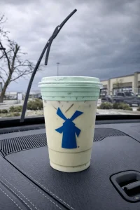 Dutch Bros Ninja Shake in a light green cup with blue windmill logo, placed on a car dashboard